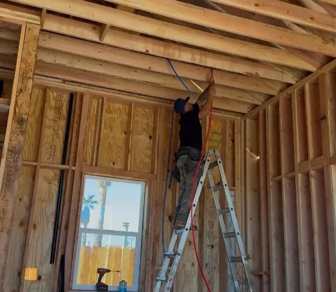 Electrician installing wiring in a wooden framed house under construction.