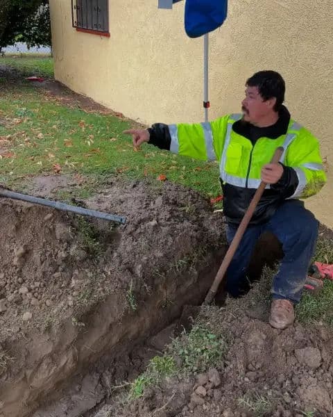 Construction worker in reflective jacket digging a trench near a building foundation.