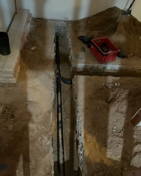 Excavated trench in a construction site with plumbing pipes and tools nearby.