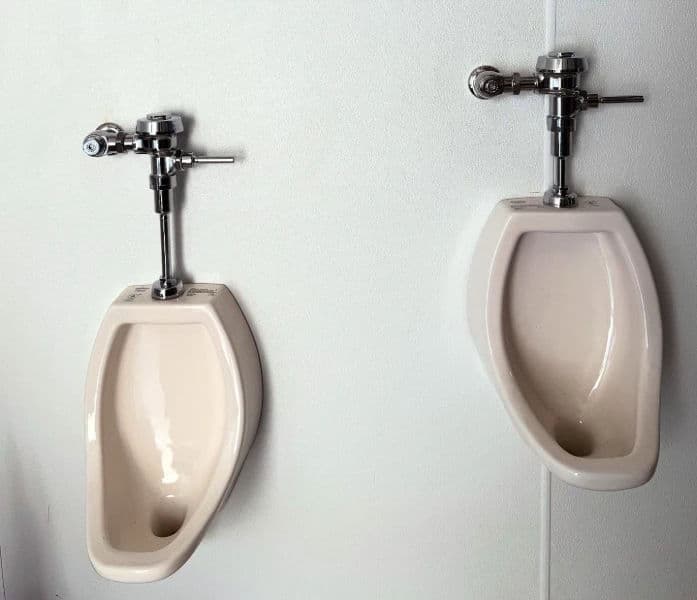 two beige urinals with chrome flush valves on a white wall