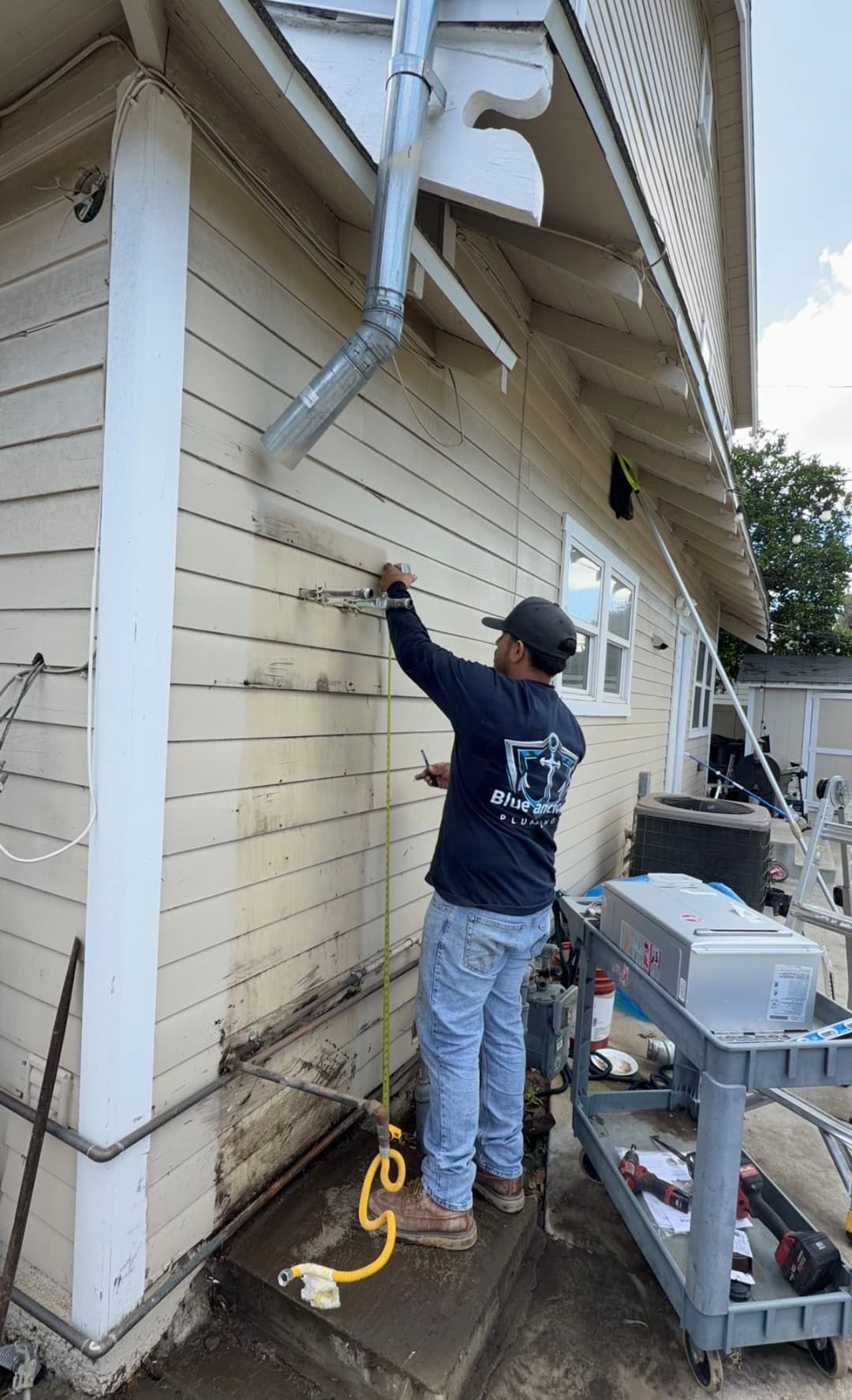 Technician cleaning building exterior with pressure washer, visible tools and equipment nearby.