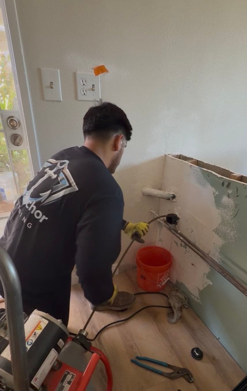 Worker repairing wall, using tools and equipment, with paint bucket nearby.