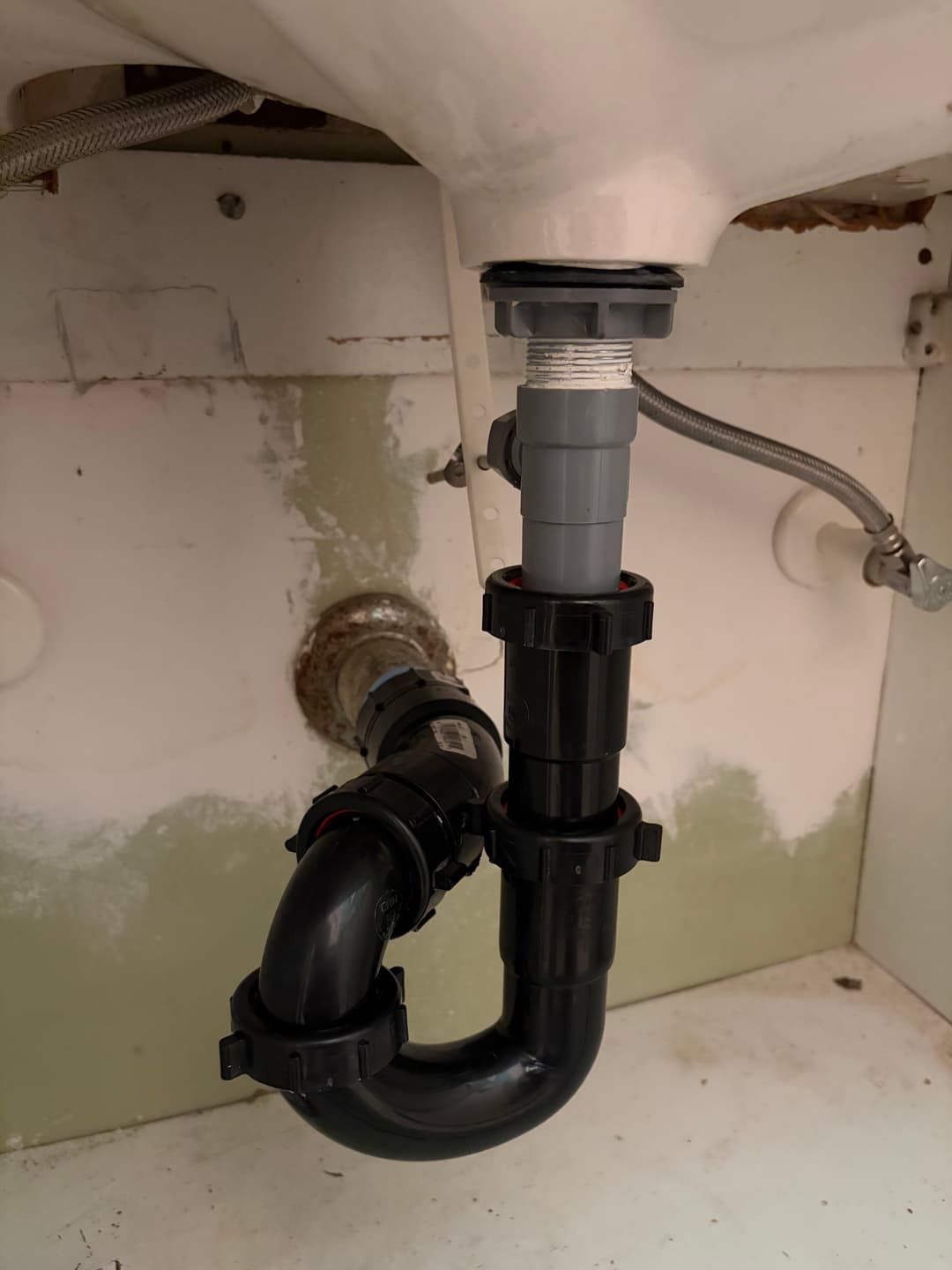 Under-sink plumbing showing a gray and black P-trap installation with visible drainage.