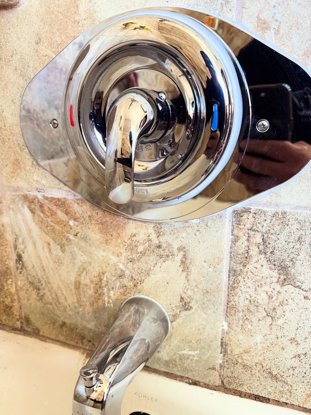 Chrome shower faucet with red and blue temperature indicators on a textured wall.