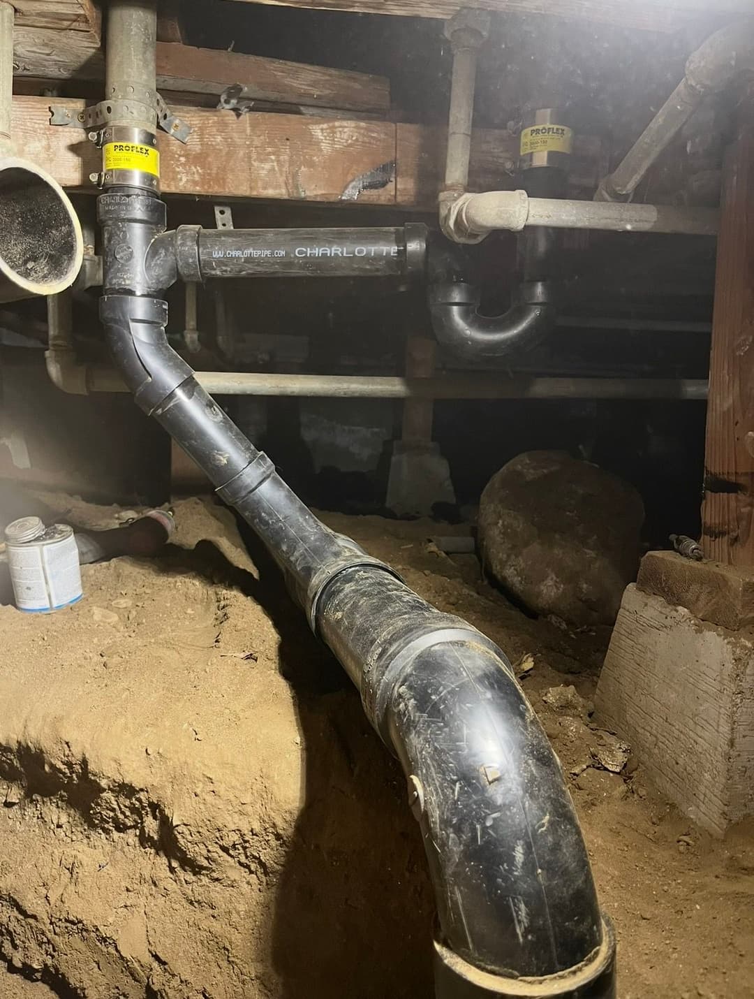 Underground plumbing system with black pipes and dirt foundation in a crawl space.