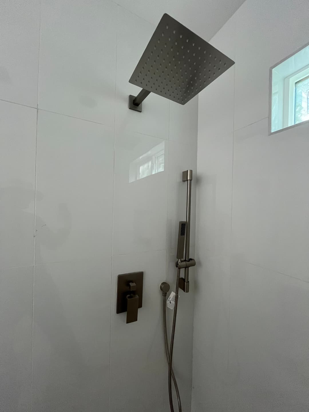 Modern shower with a large rainfall showerhead and handheld sprayer in sleek white tiles.