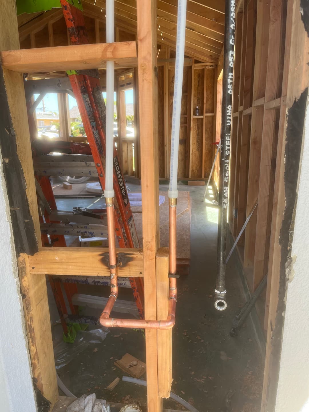 Exposed copper plumbing in a partially constructed home with framed walls and ladders.