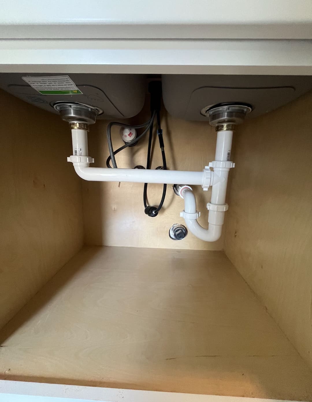 Under-sink plumbing with PVC pipes and sink drain connections in a wooden cabinet.