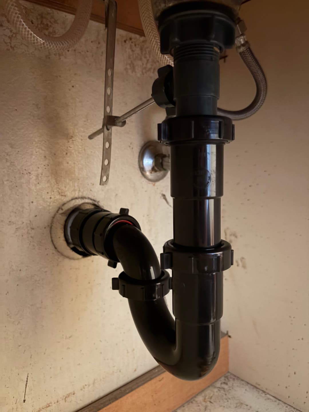 Under-sink plumbing with black PVC pipe and drainage connection.