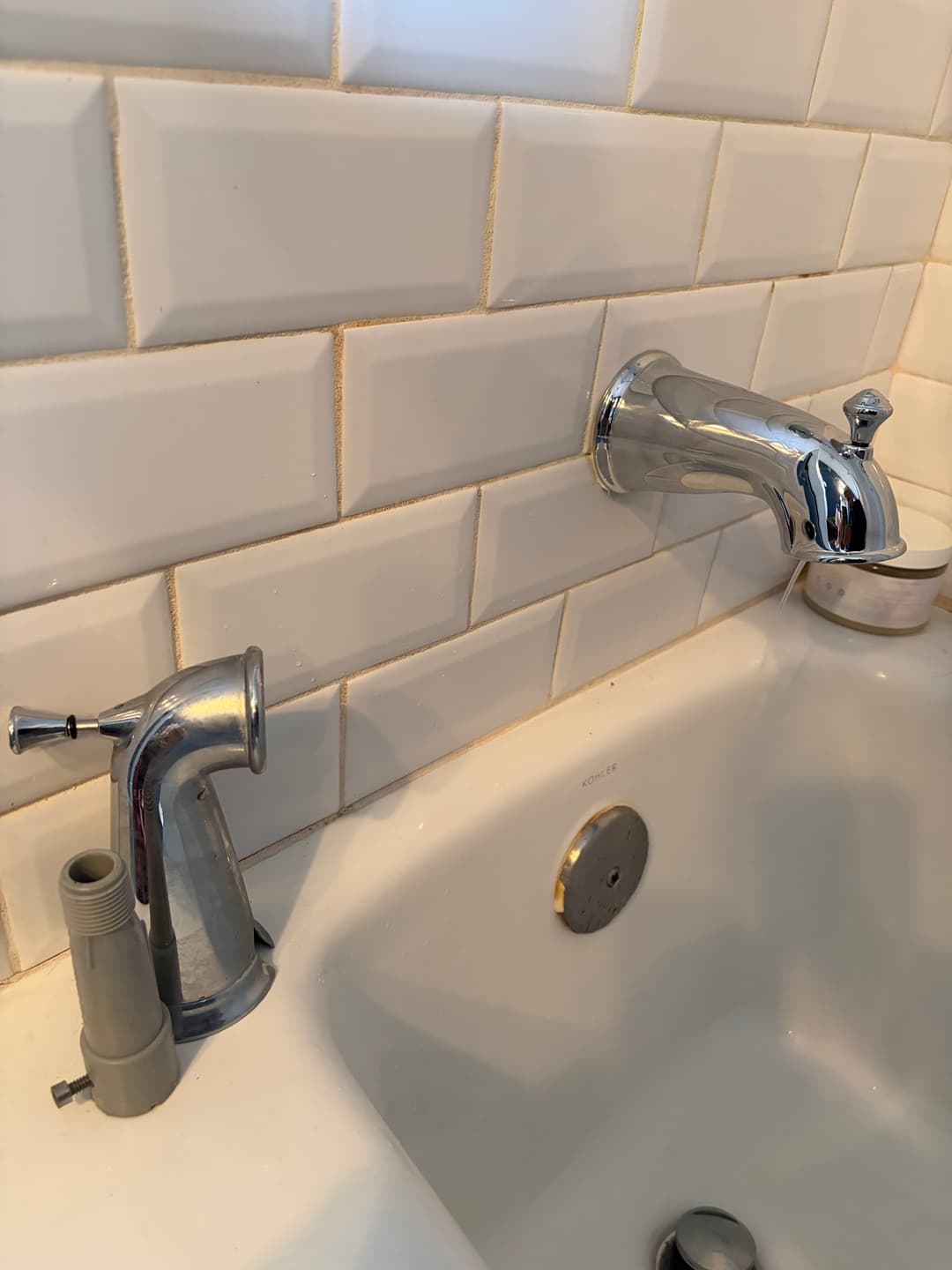 Modern bathtub faucet and diverter against a white tiled wall.