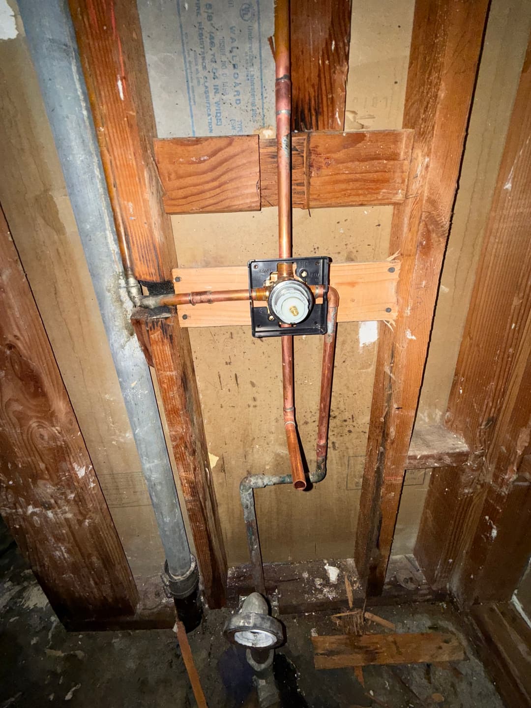 Copper plumbing installation on wooden studs in a wall, showcasing pipes and valve connections.