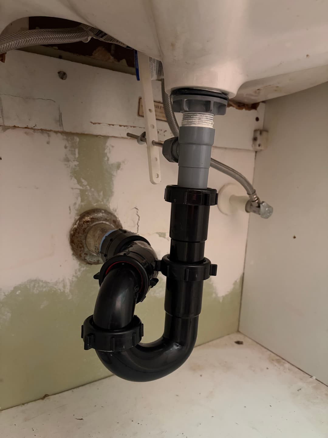 Under-sink plumbing installation showcasing black PVC pipe and fittings.