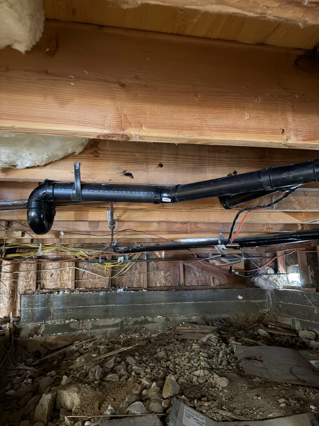 View of plumbing pipes and electrical wiring in a residential crawl space.