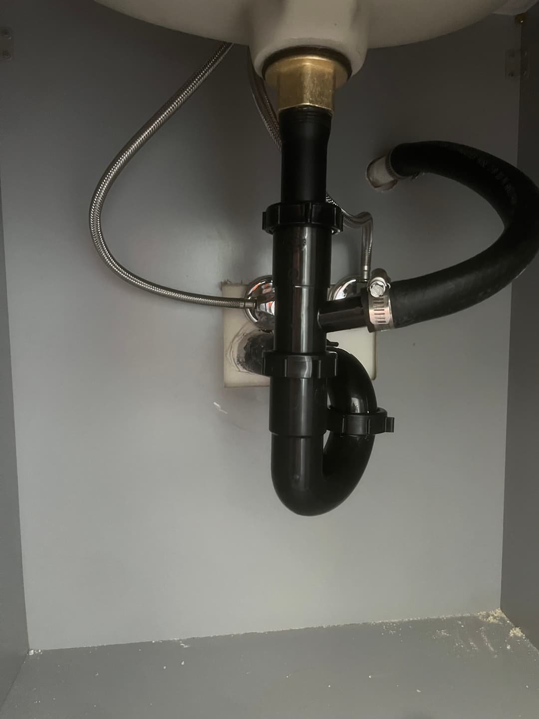 Plumbing under sink with black and silver pipes and fittings.