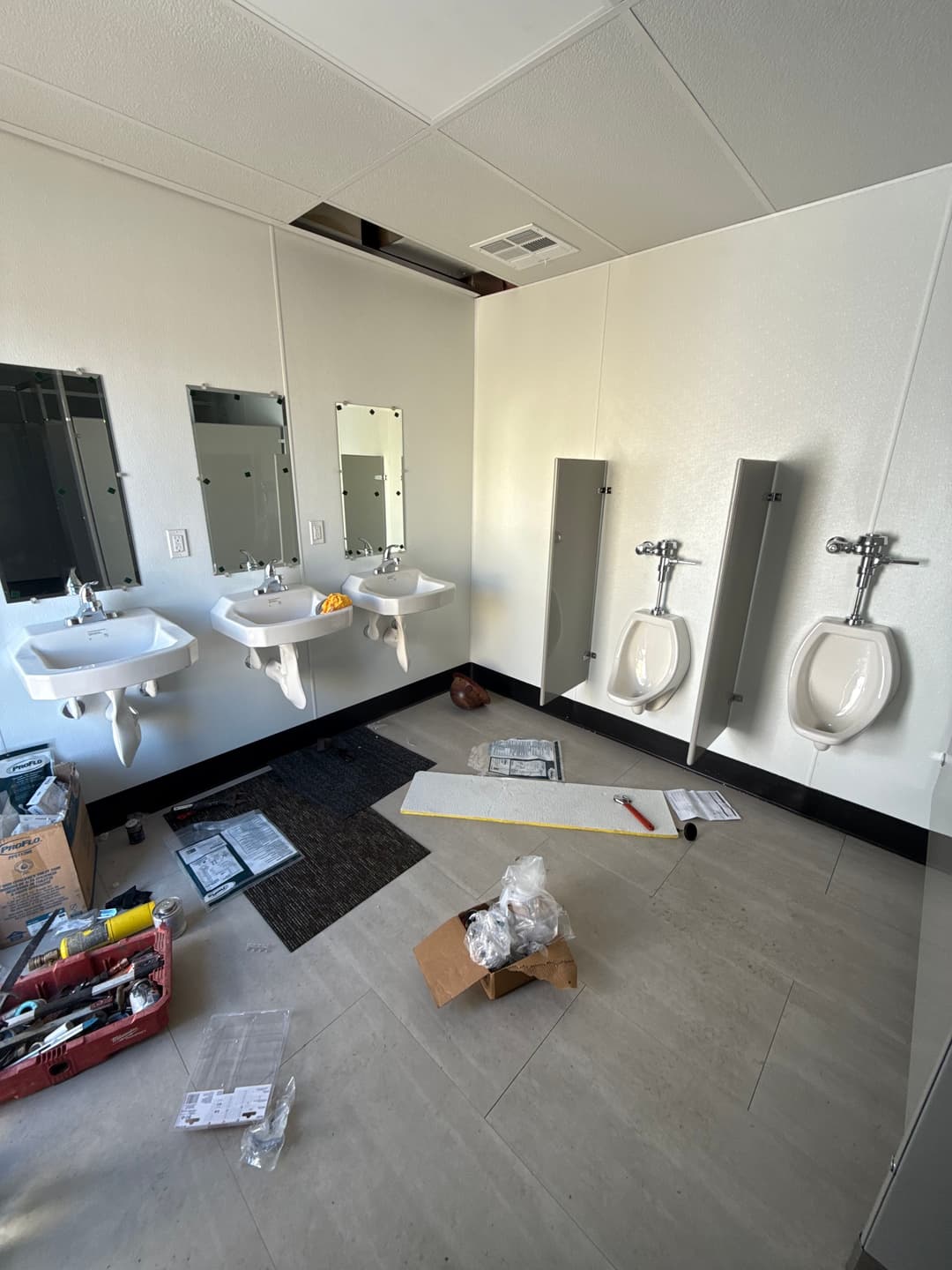 Bathroom under renovation with two sinks, urinals, and construction materials on the floor.