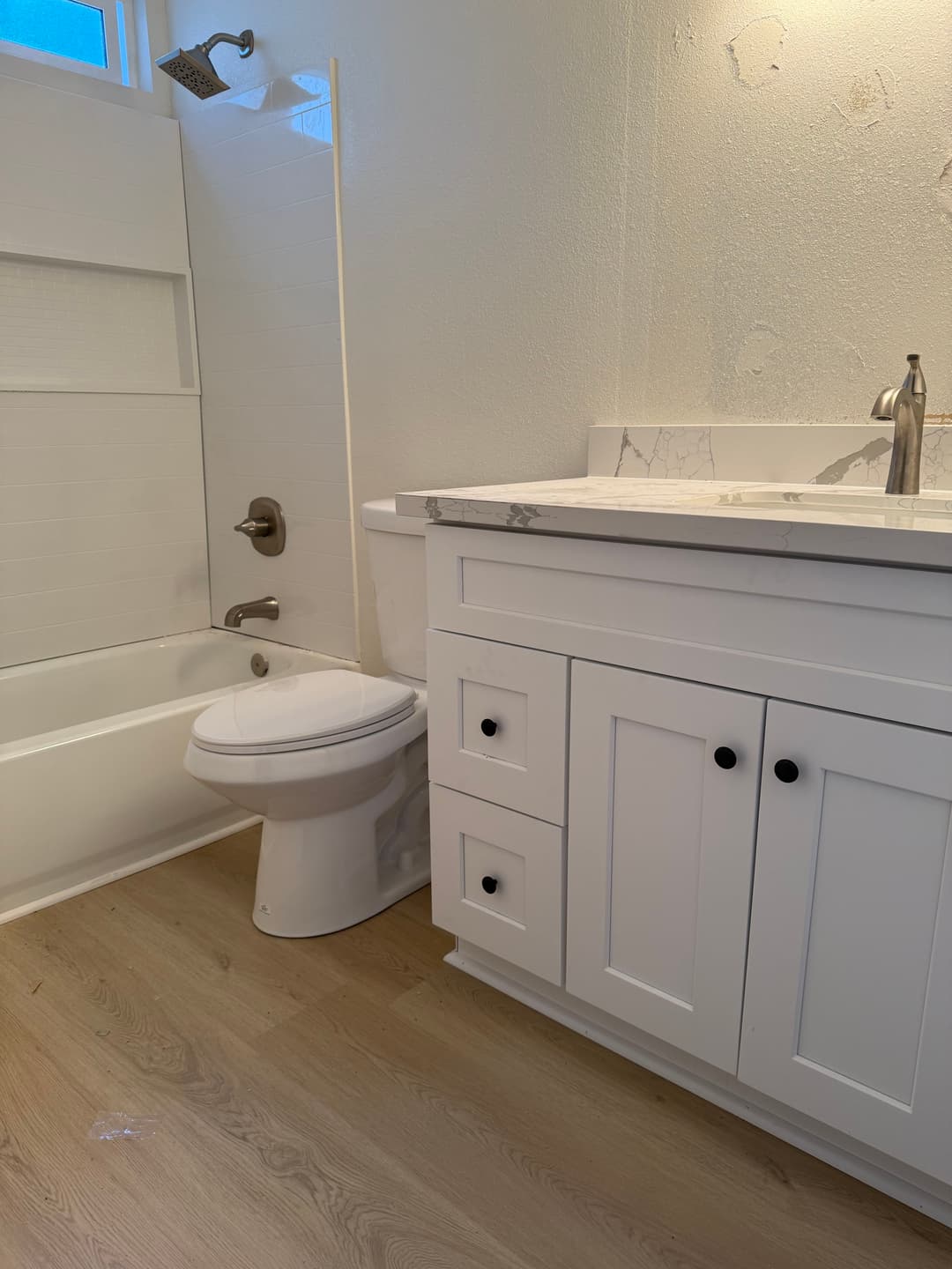Modern bathroom featuring a white vanity, tub, and neutral wood flooring. Clean and bright design.
