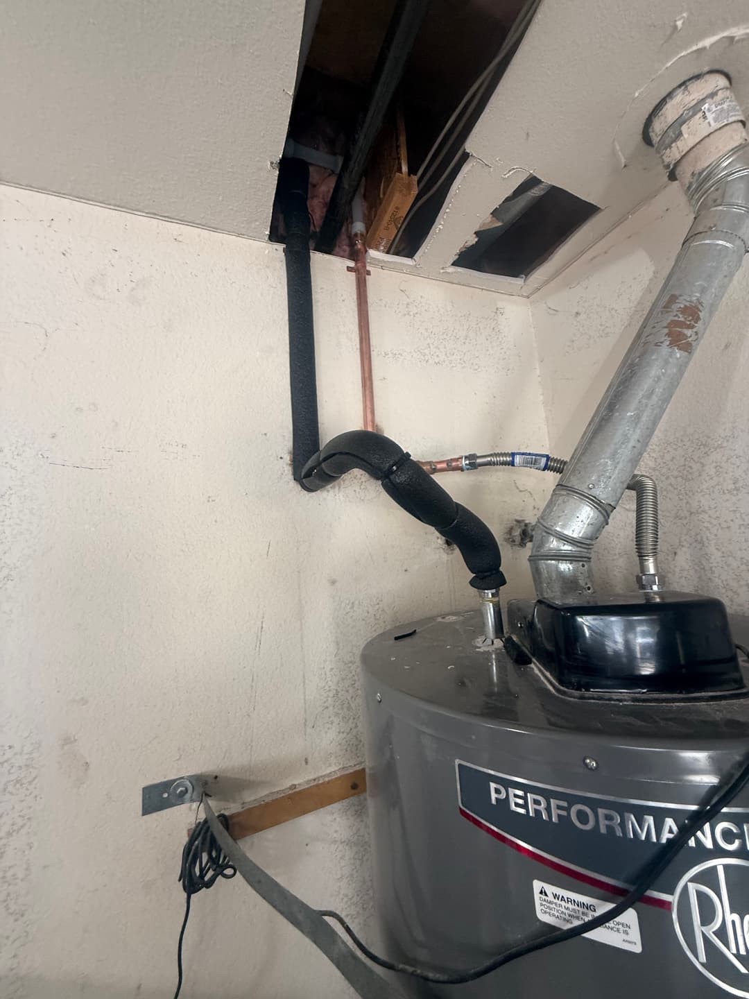 Water heater installation with exposed pipes and ceiling damage in a utility room.
