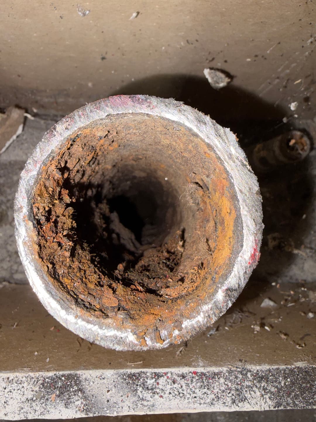 Rusty, corroded pipe interior showing buildup and deterioration in a residential setting.