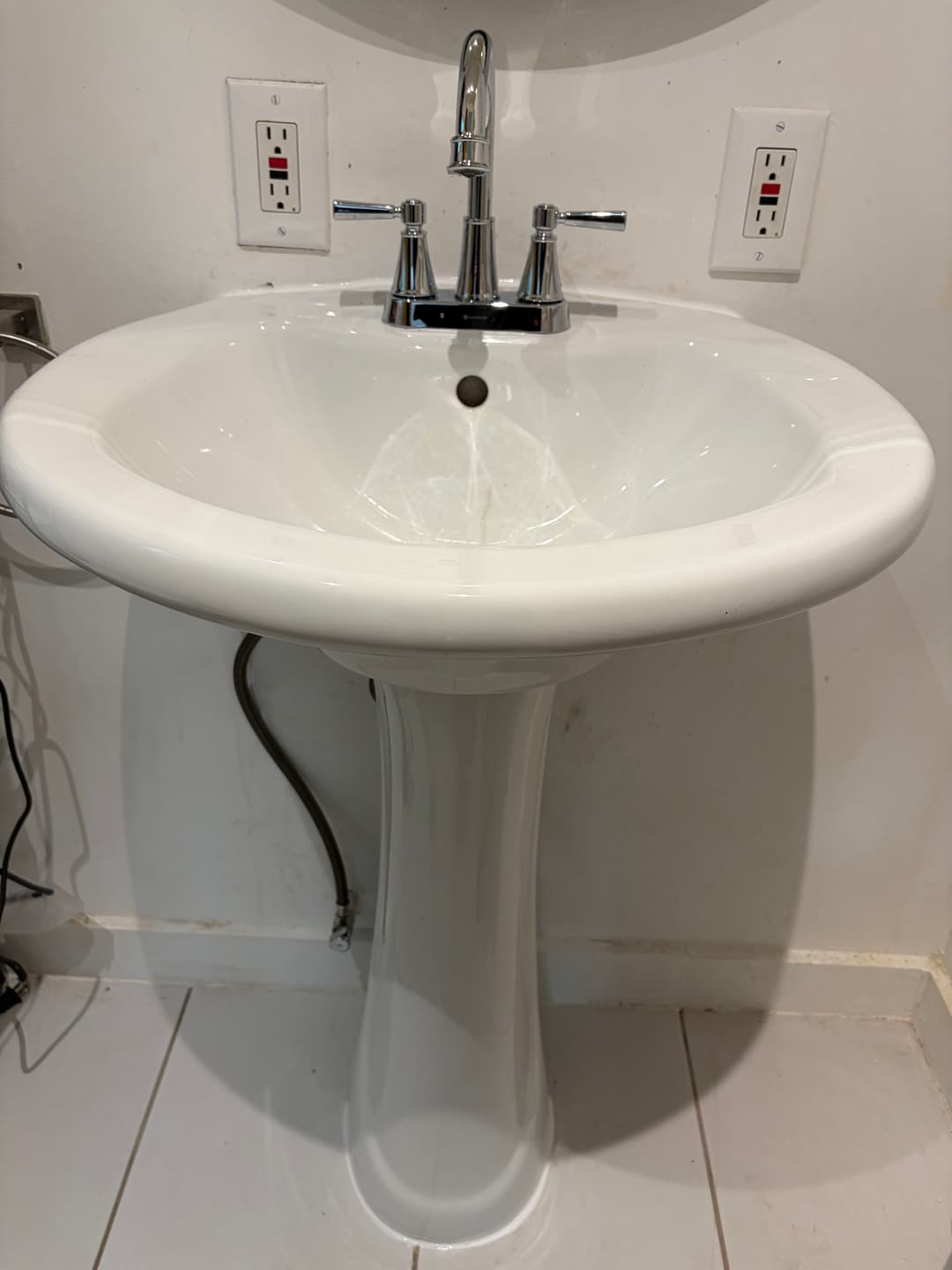 White pedestal sink with chrome faucet, mounted on a tiled wall.