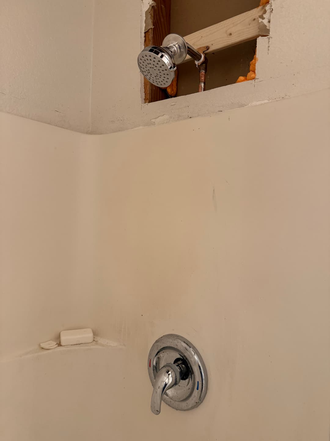 Shower fixture with exposed plumbing and hole in wall for renovation.