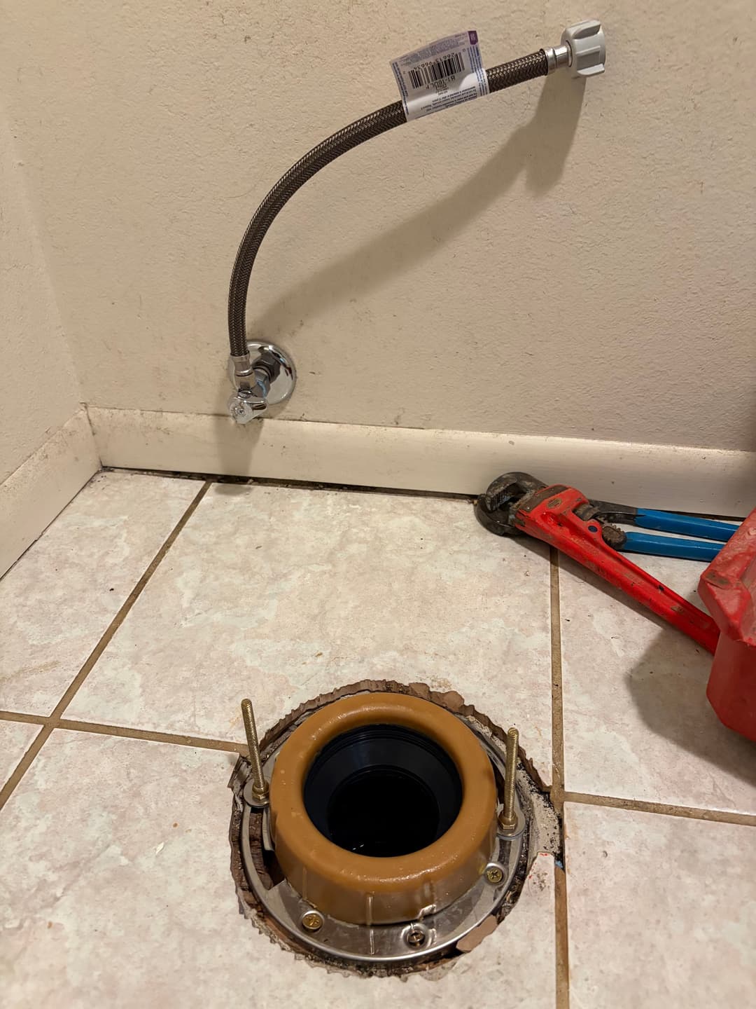 Plumbing installation with a floor flange, water supply line, and tools on tiled surface.