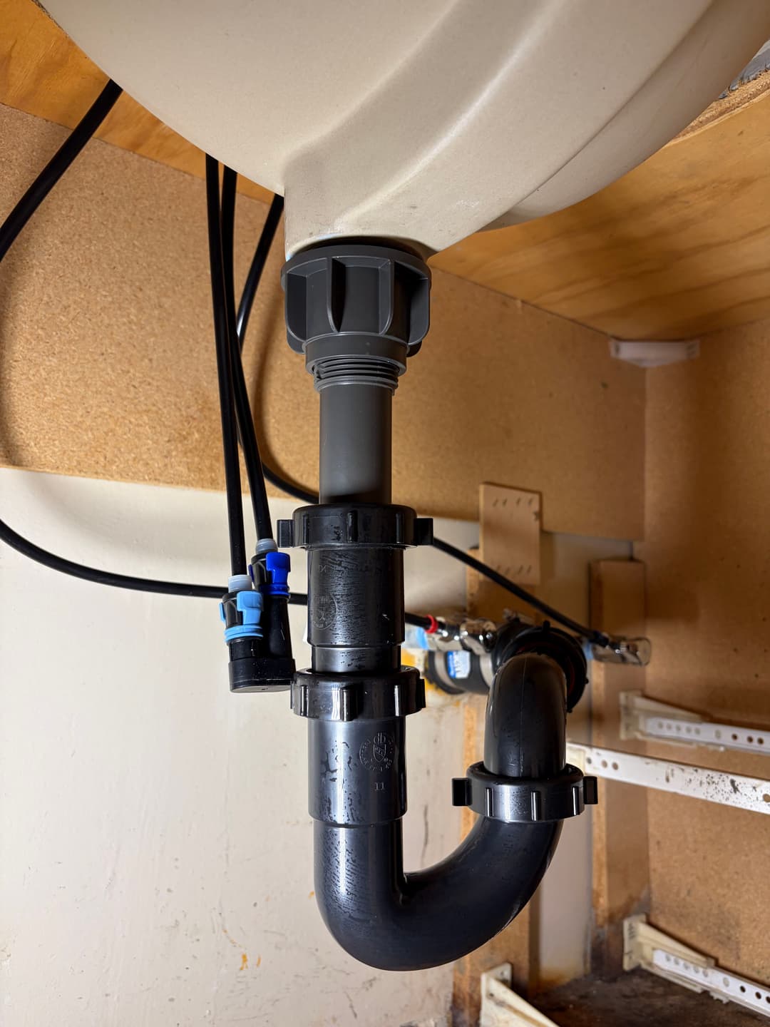 Under-sink plumbing with PVC pipes, connectors, and a P-trap assembly.