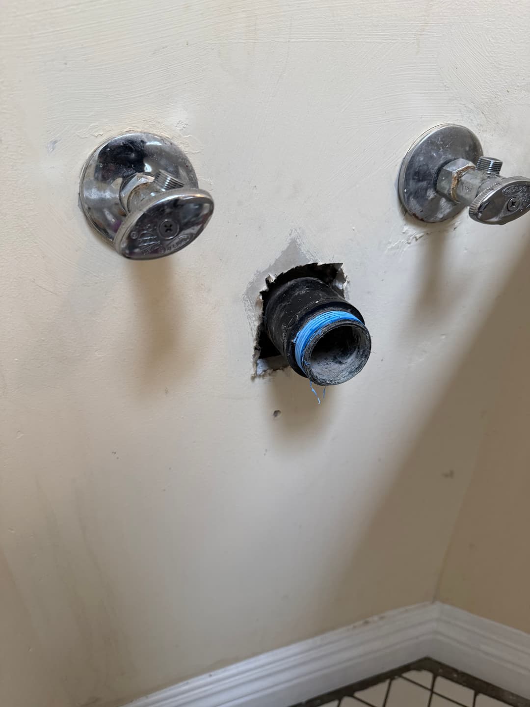 Wall plumbing setup with exposed pipe, two valves, and surrounding wall damage.