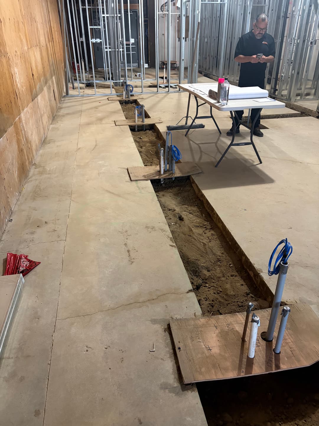 Construction site with exposed plumbing, framing, and a worker reviewing plans at a table.