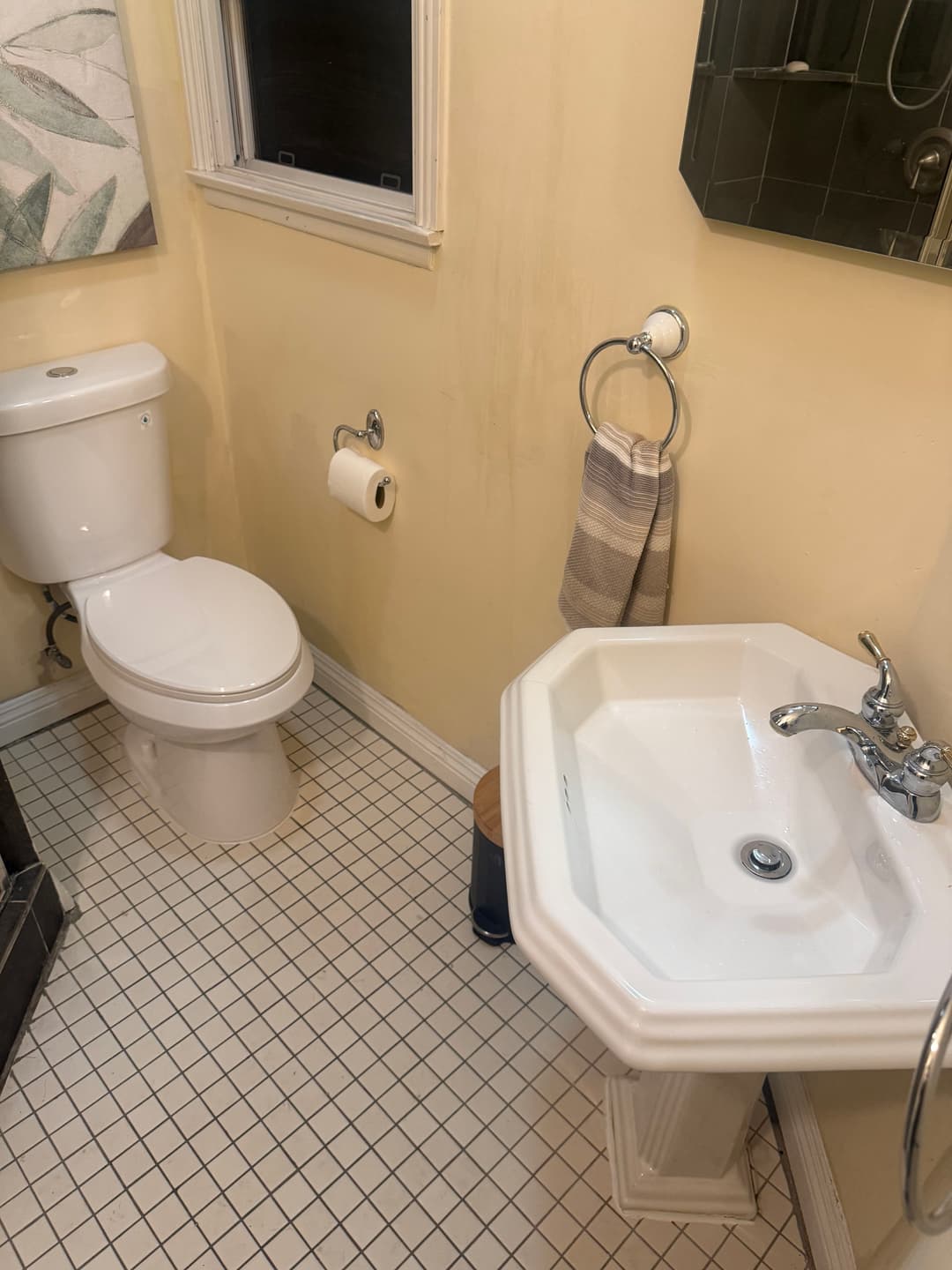 small bathroom with a toilet, pedestal sink, and wall mirror in light-colored decor