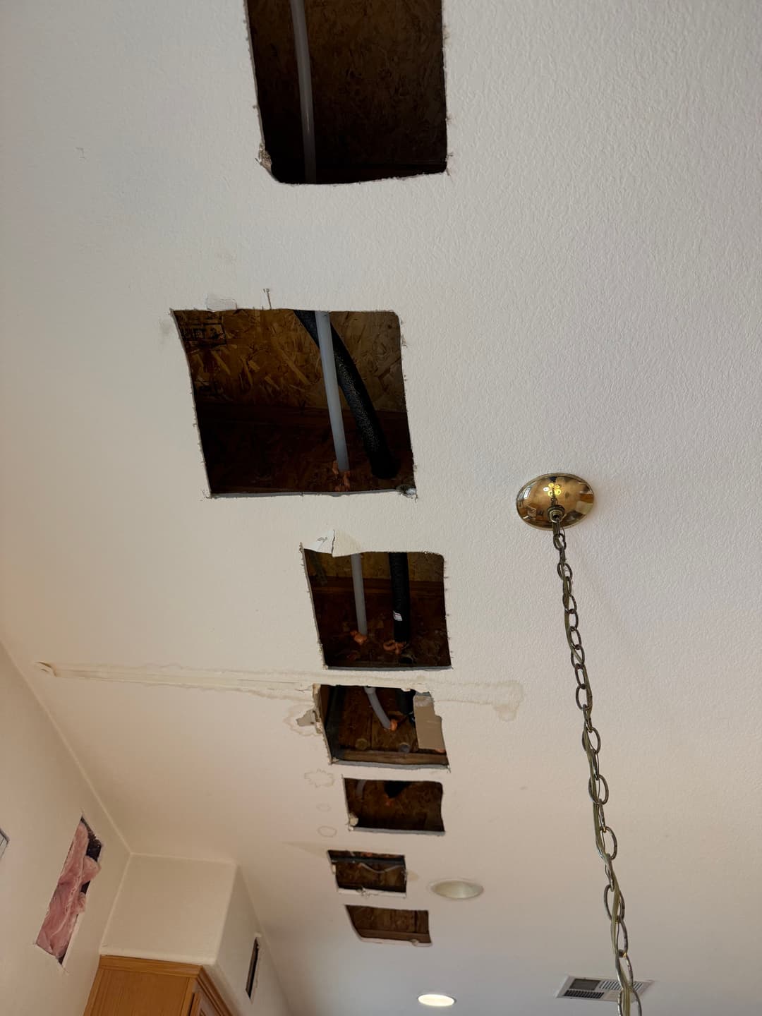 Exposed ceiling with cutouts revealing plumbing and electrical work above.