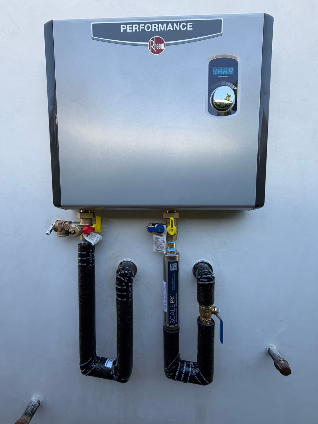 Rheem performance tankless water heater with plumbing connections mounted on a wall.