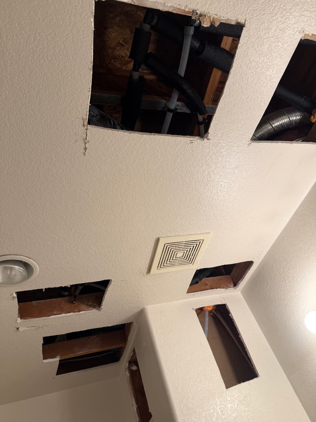 Exposed ceiling sections revealing plumbing and ventilation in a bathroom renovation.