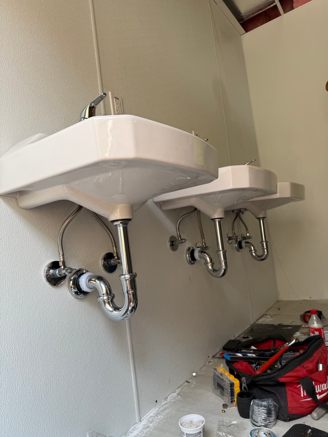 Wall-mounted sinks with chrome plumbing in a construction setting.