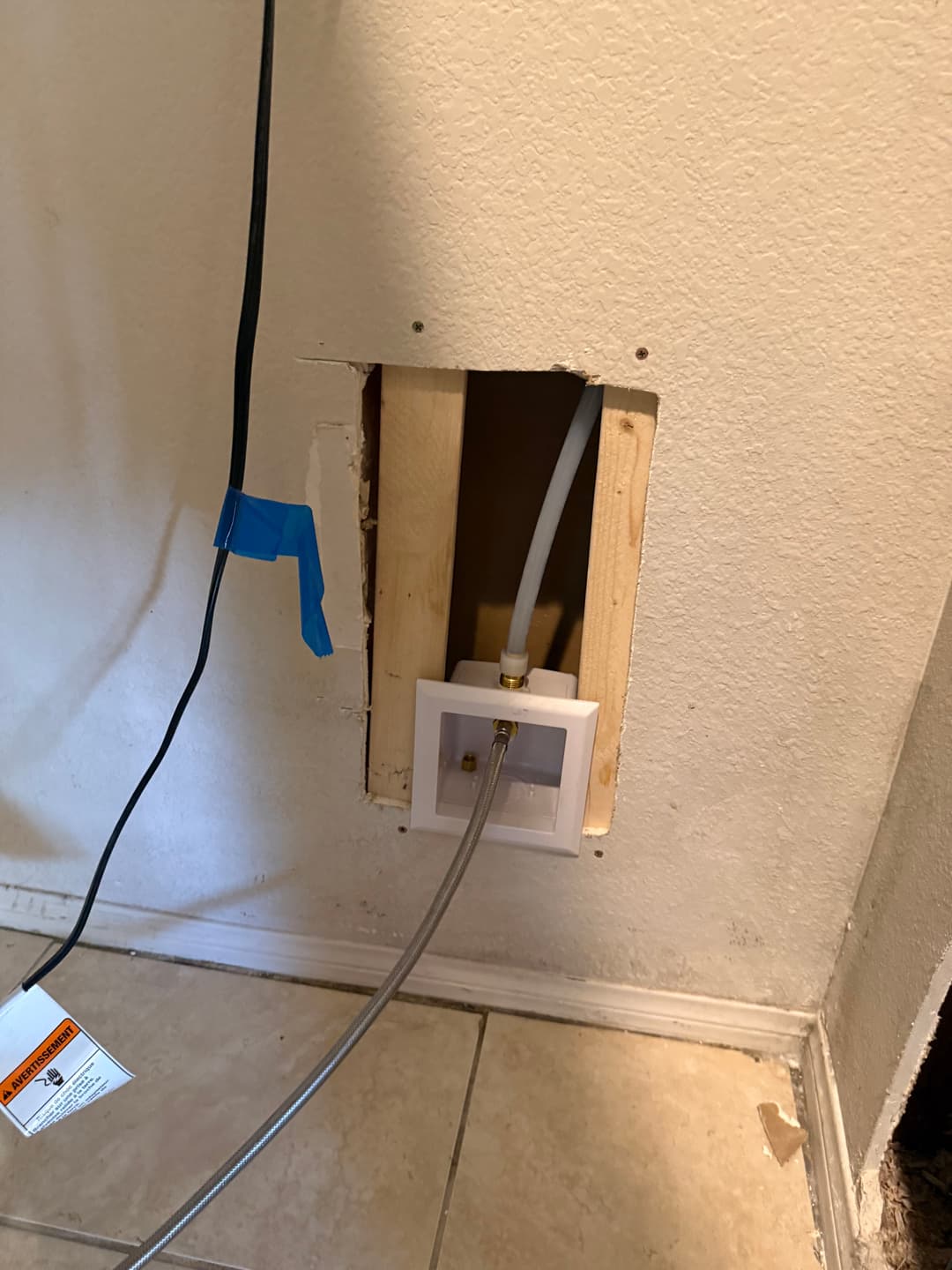 Cutout in wall showing water line connection for refrigerator installation.