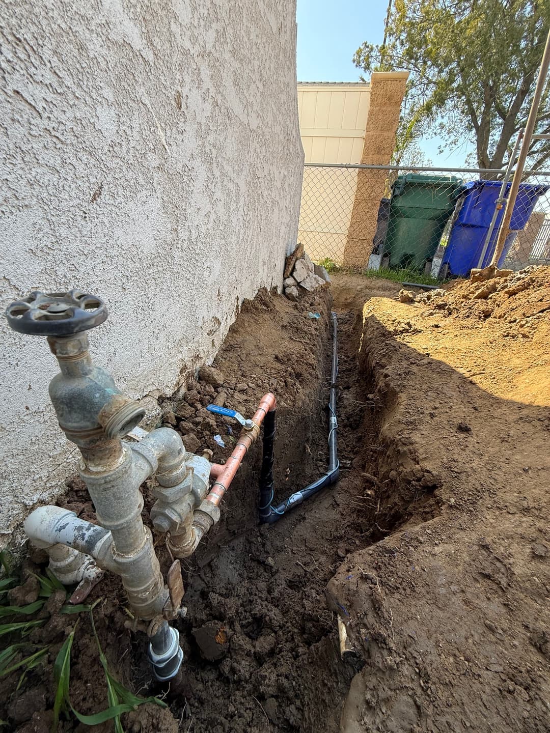 Exposed water pipes in trench near a house, showcasing plumbing installation work.