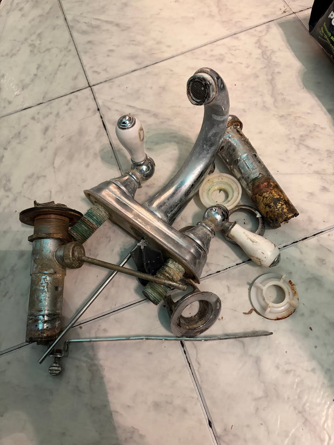 Rusty plumbing fixtures and faucets arranged on a tiled floor.