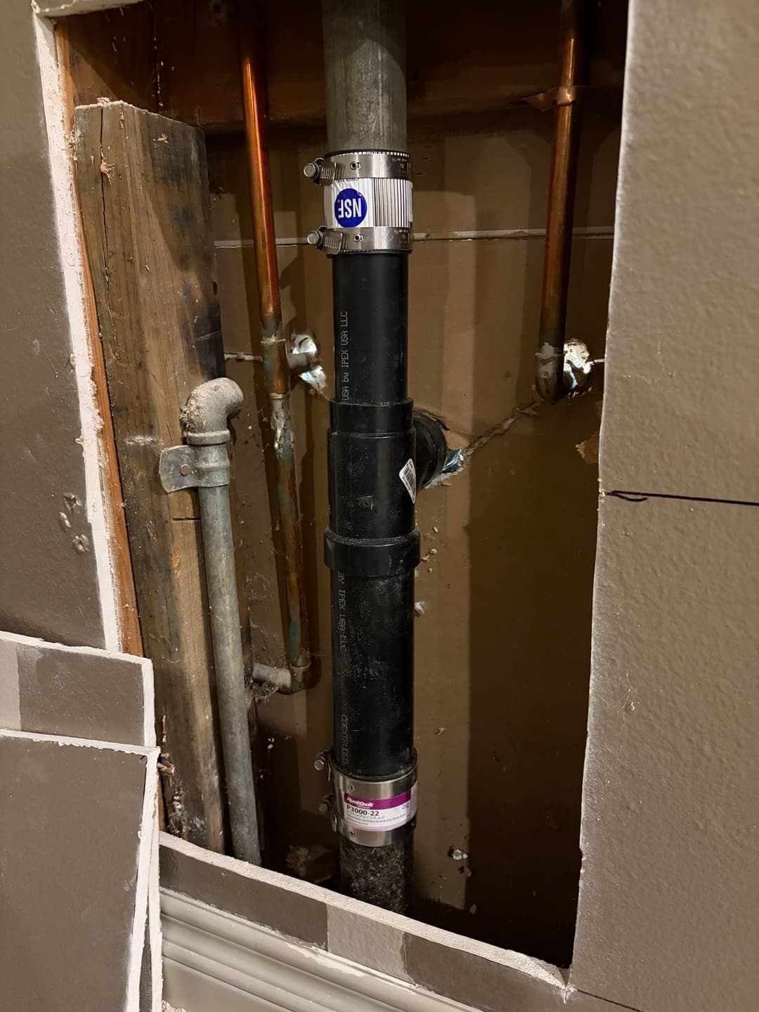 Visible plumbing pipe installation behind a wall, showcasing copper and PVC piping.