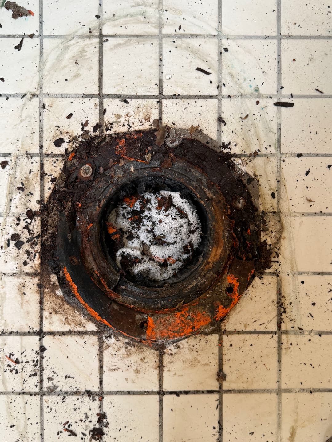 Dirty shower drain with rust and debris on tiled floor. Maintenance needed for plumbing.