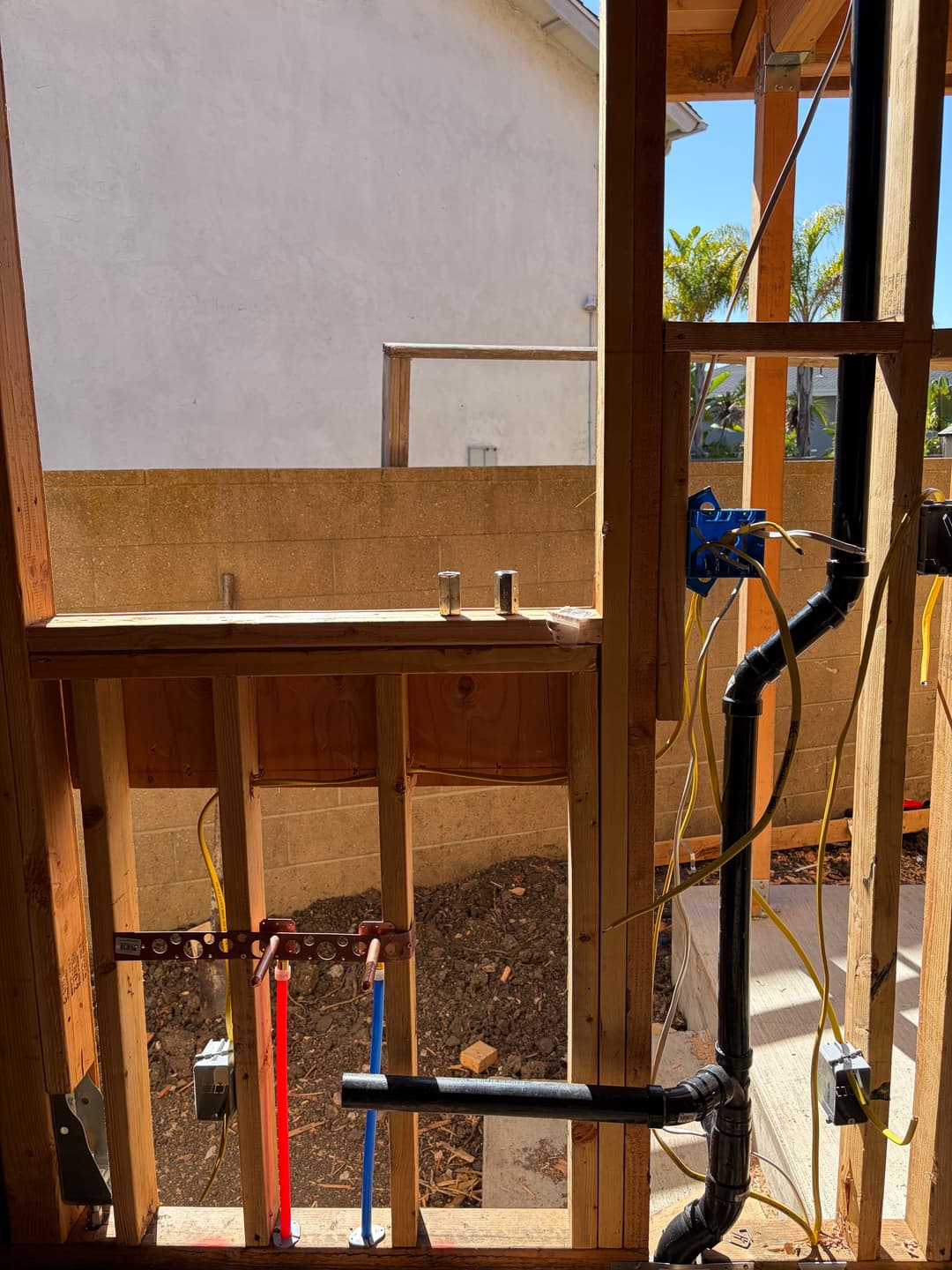 Construction view through framed wall with plumbing and electrical work visible.