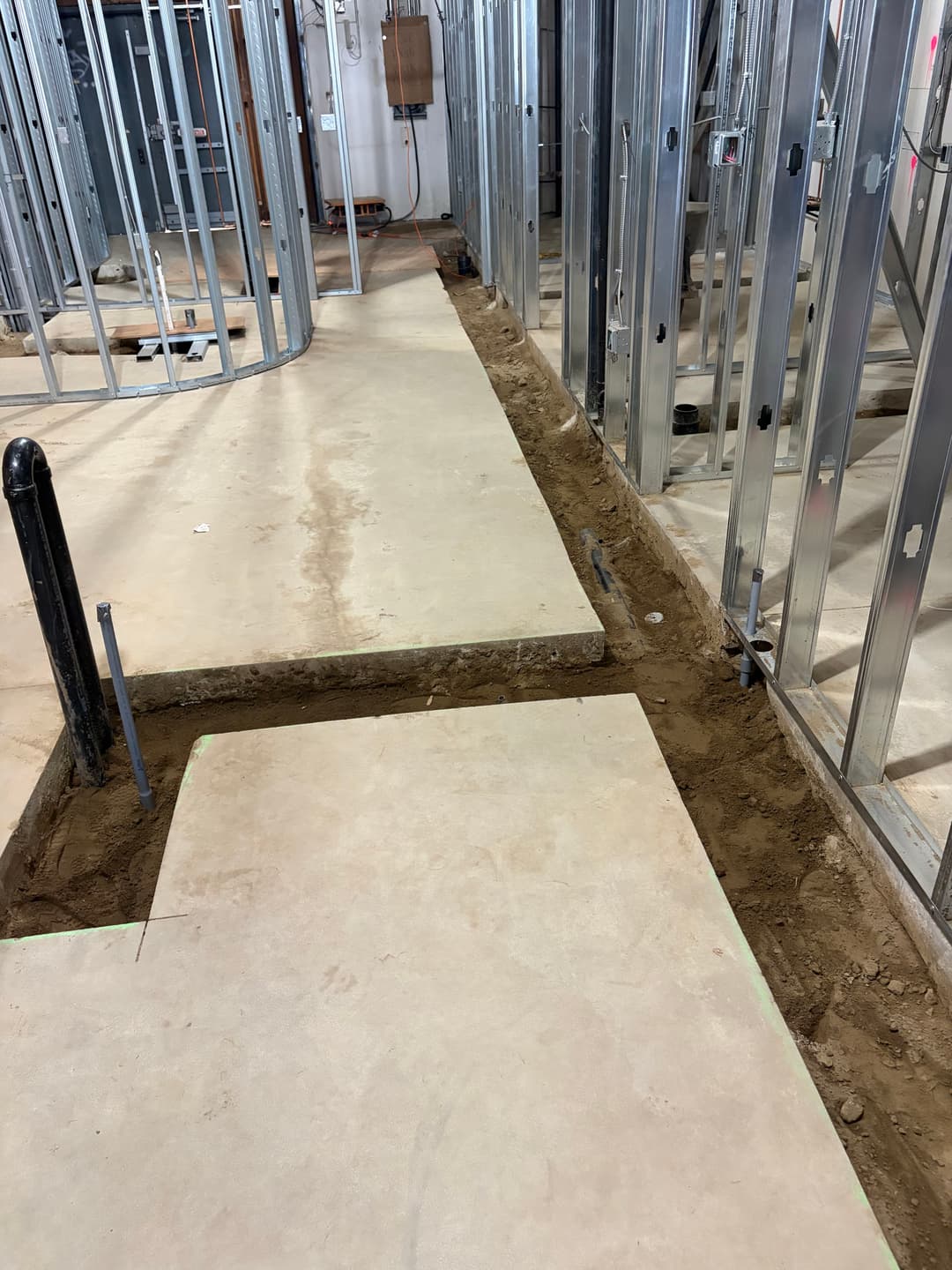 Construction site showing a trench in concrete flooring with metal framing in the background.