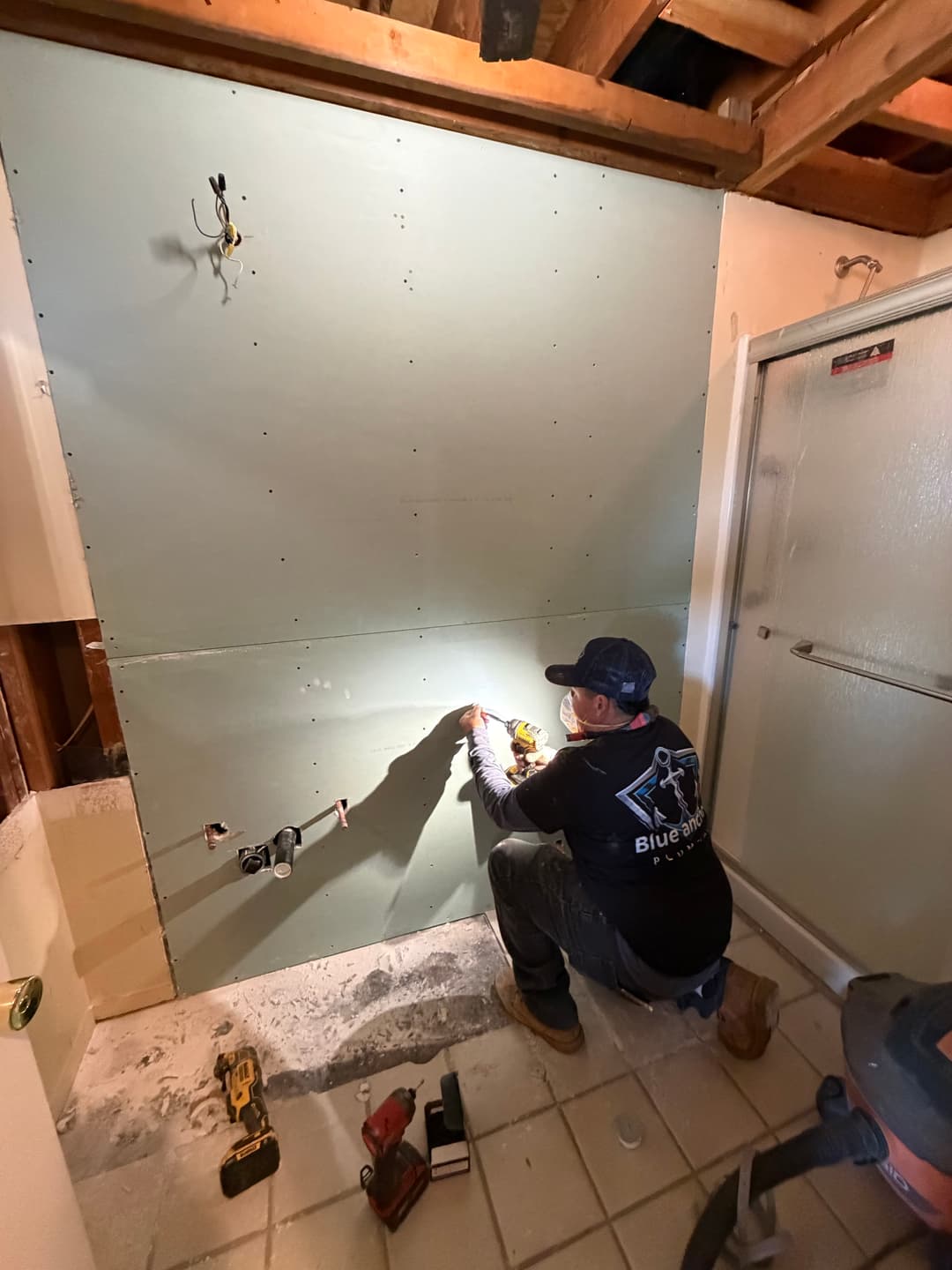 Contractor installing drywall in a bathroom renovation project, tools and shower visible.