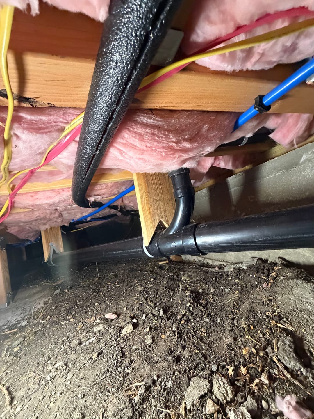 Pipes and insulation in a crawl space, showing plumbing and structural details.