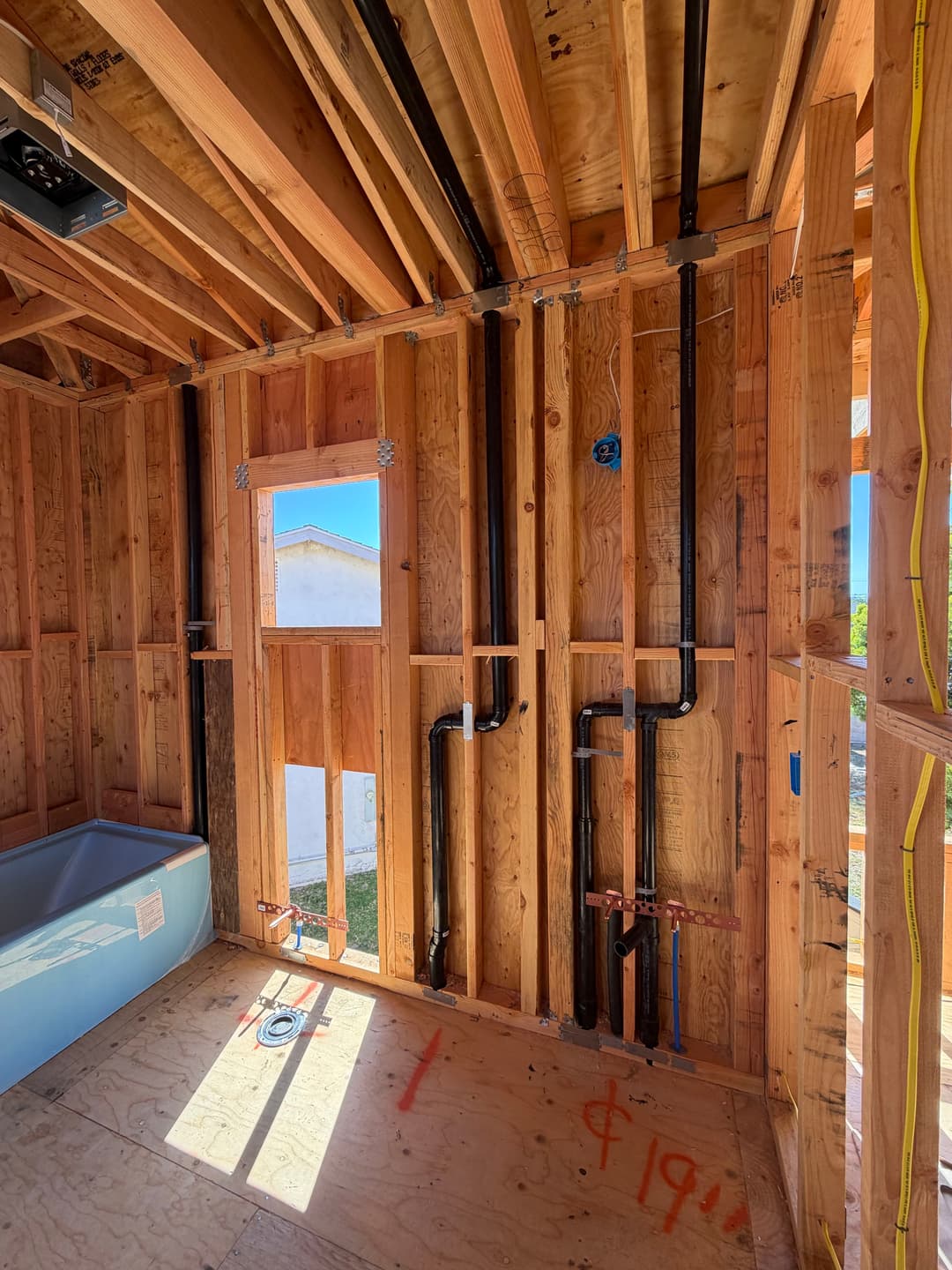 Framed bathroom interior showing plumbing and electrical work during construction.