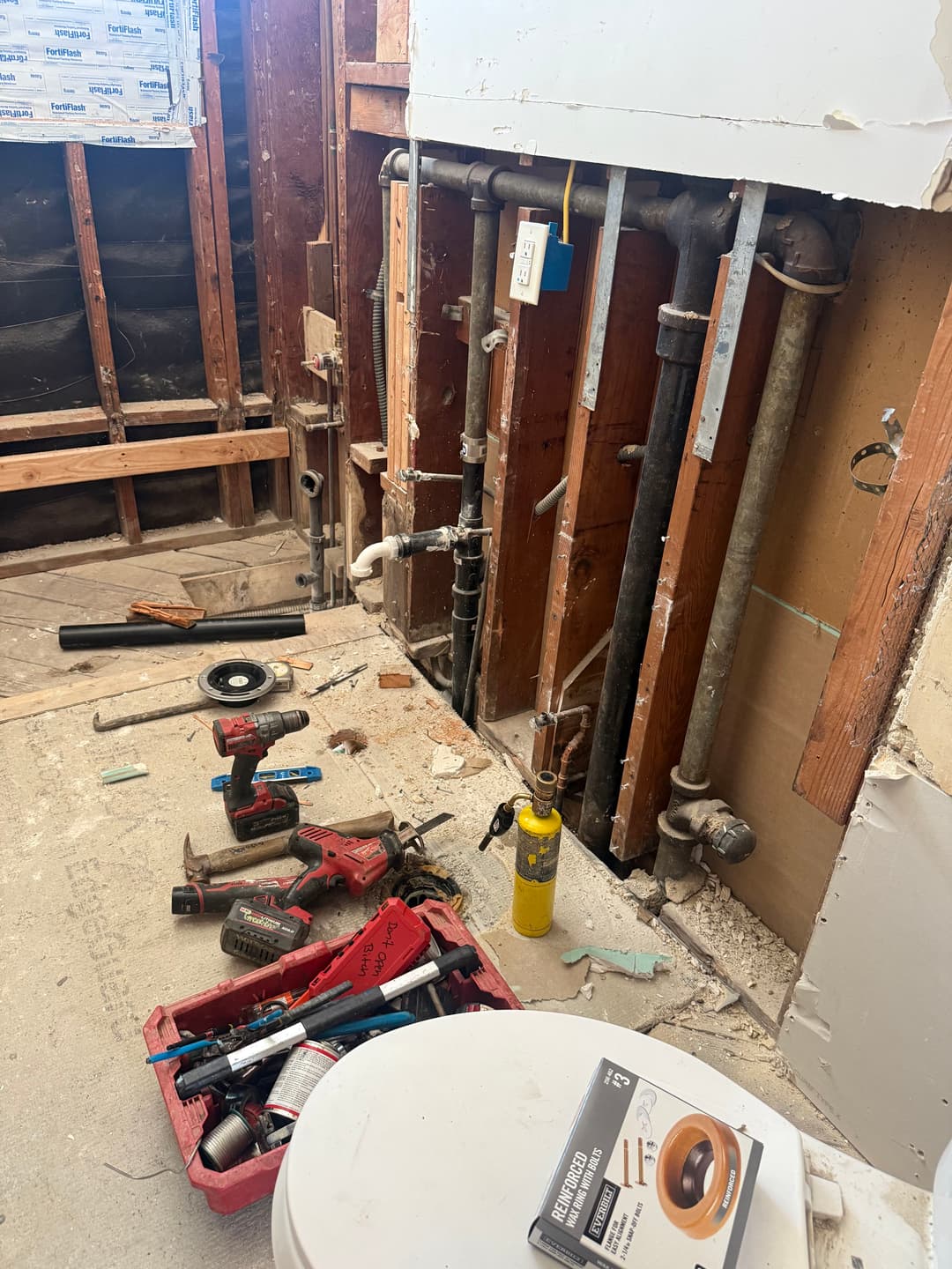 Plumbing renovation in a bathroom with tools, exposed pipes, and construction debris.