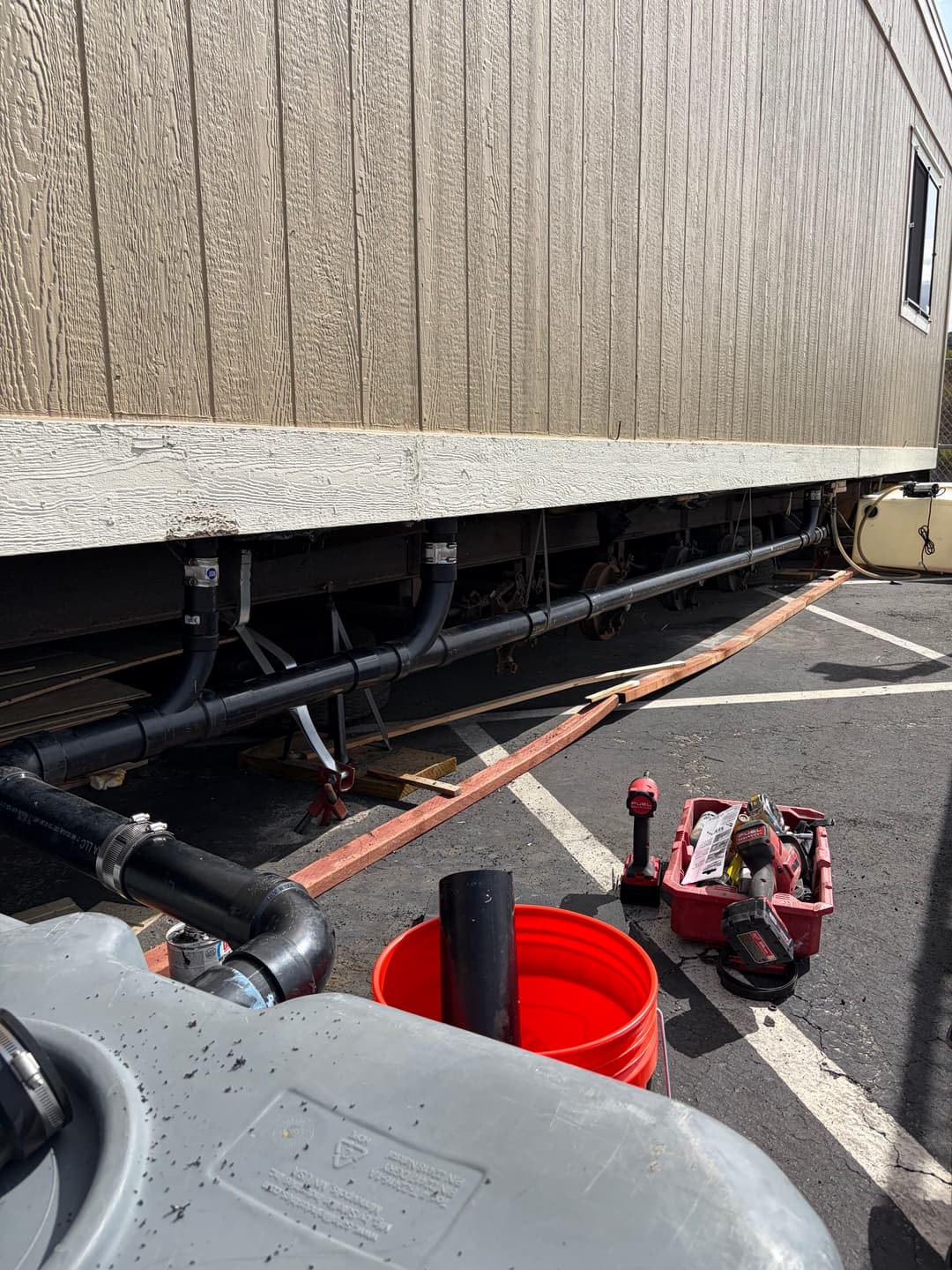 View of plumbing under a mobile home with tools and equipment for repairs.