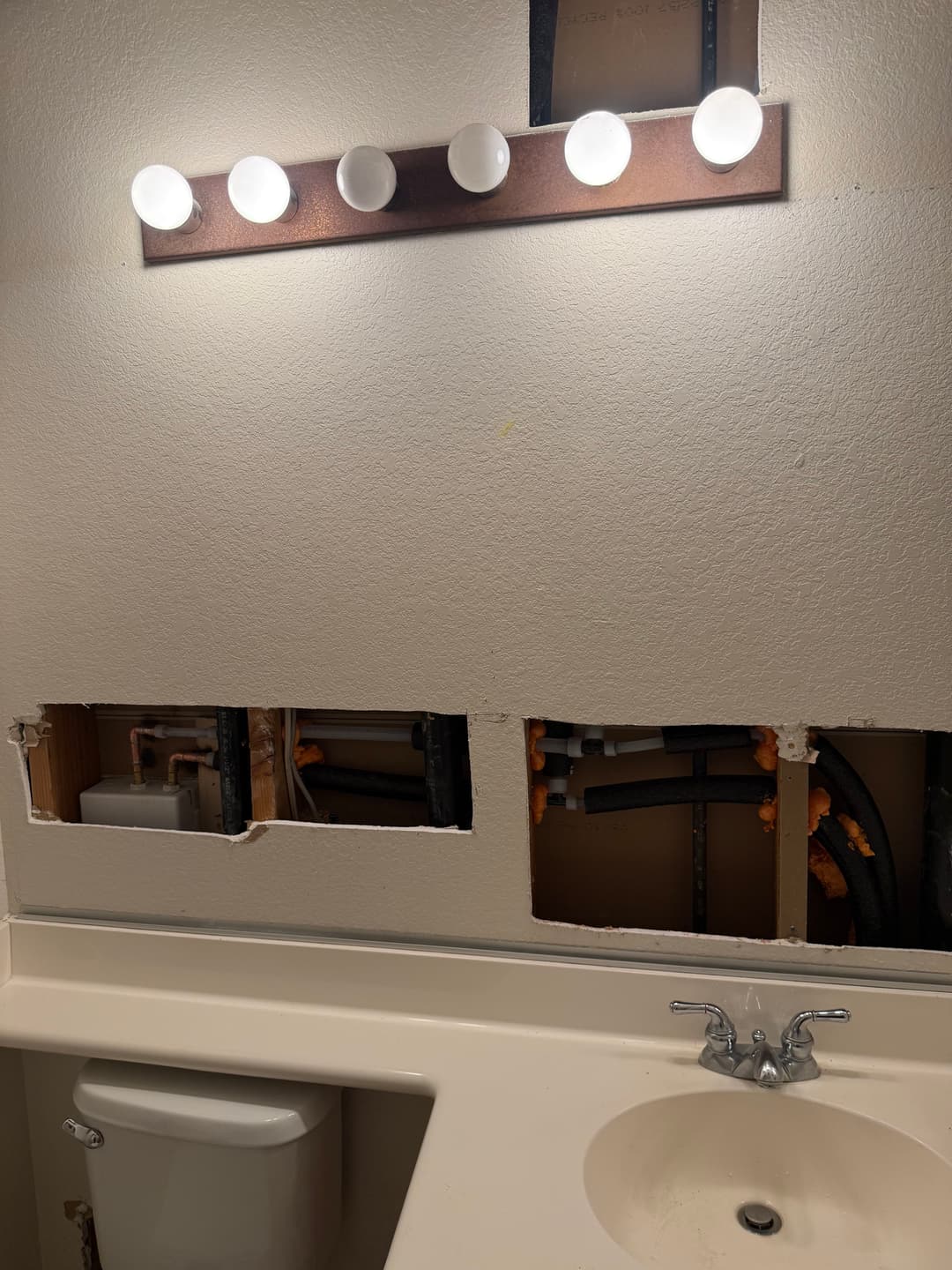 Bathroom renovation with exposed plumbing and lighting fixture above the vanity.