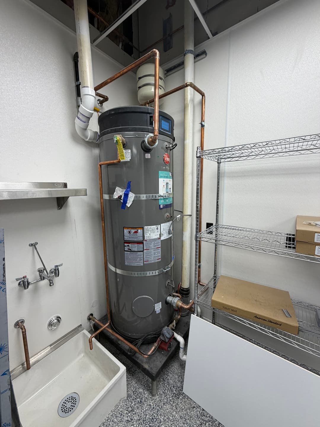 Water heater installation in a utility room with copper piping and drainage.