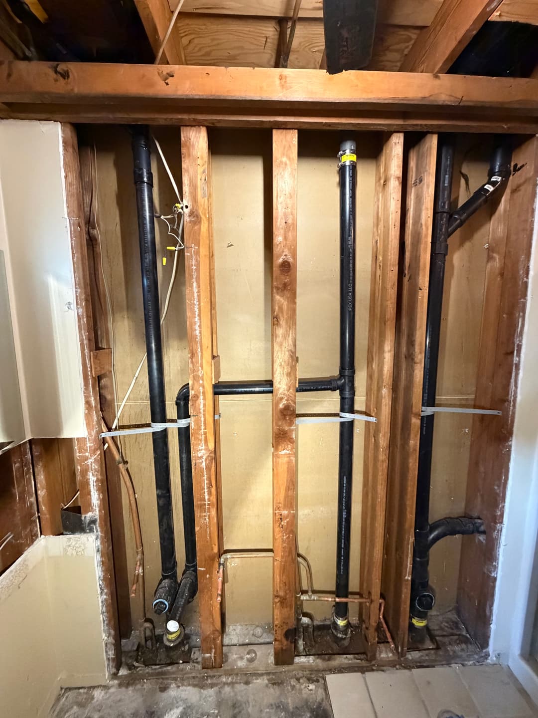 Exposed plumbing pipes in a renovated wall, showcasing plumbing installation and framing details.
