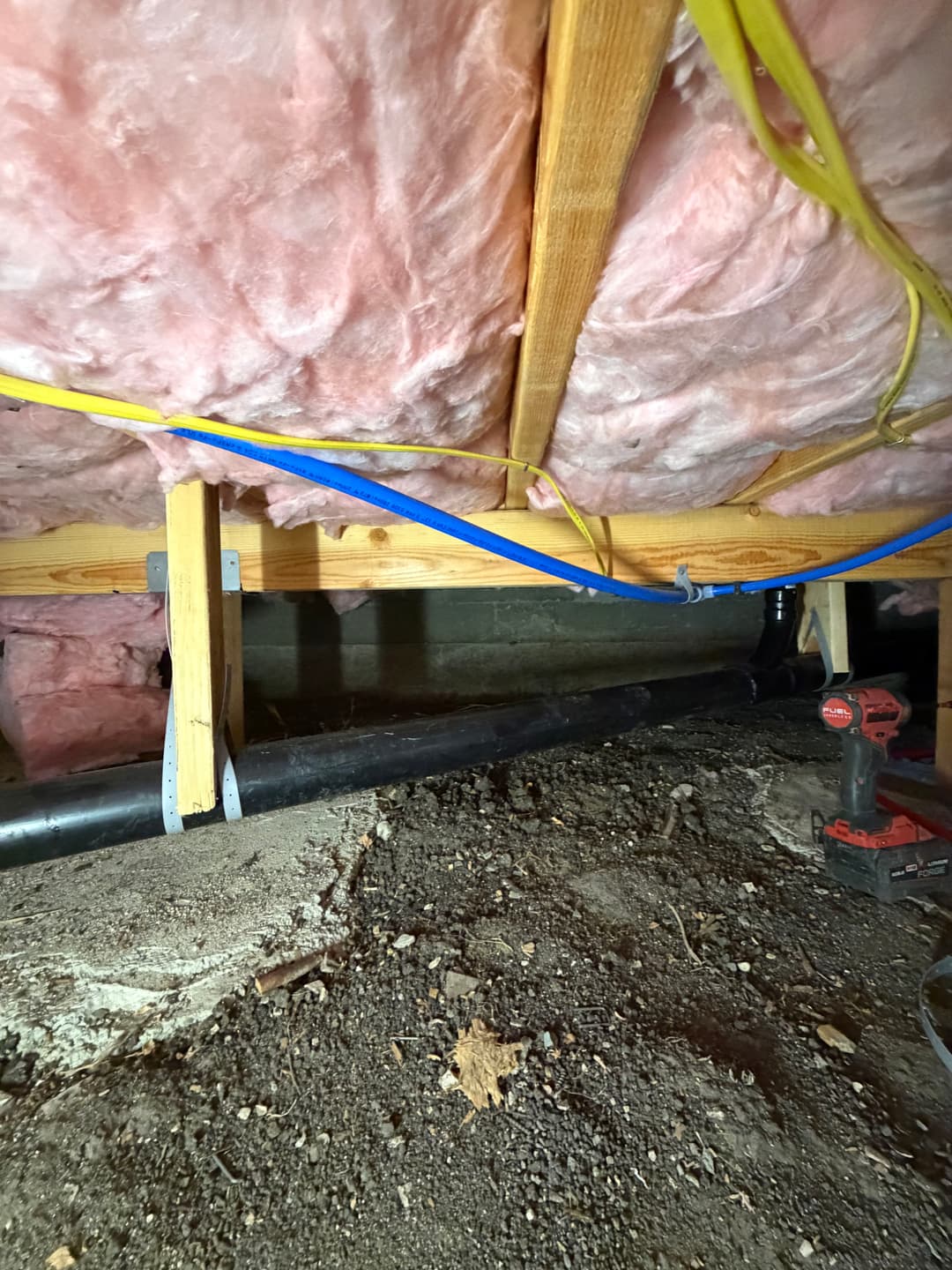 Underneath a home with insulation and plumbing, showcasing construction details.