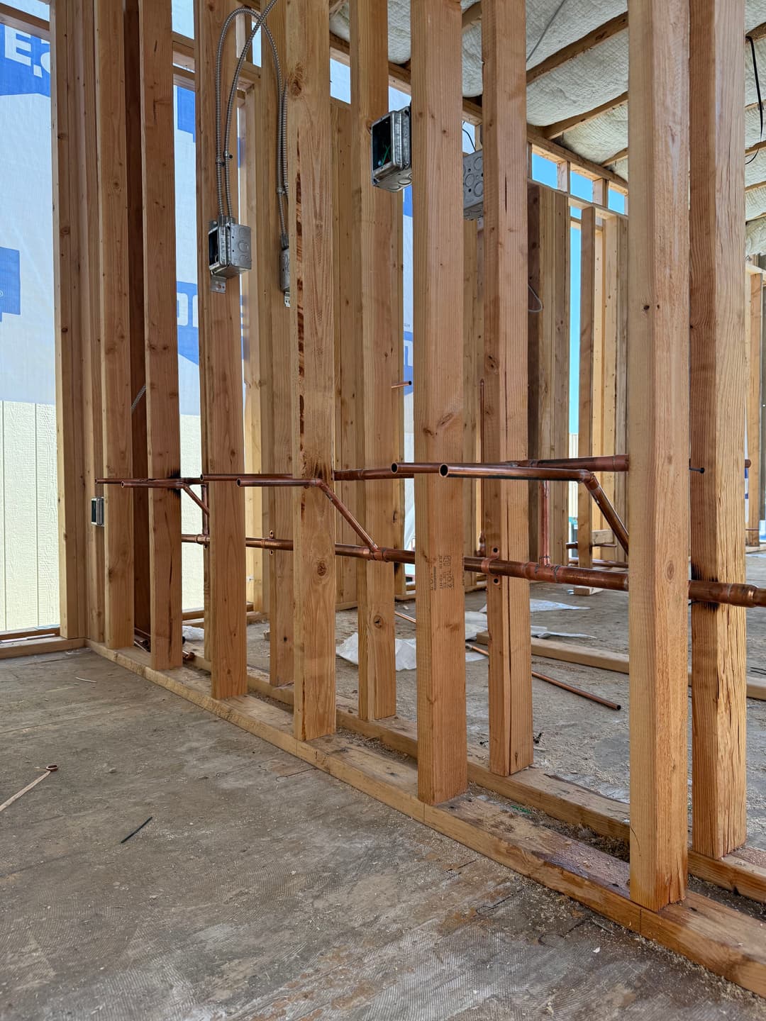 Framing of new construction with exposed wood studs and copper plumbing pipes.